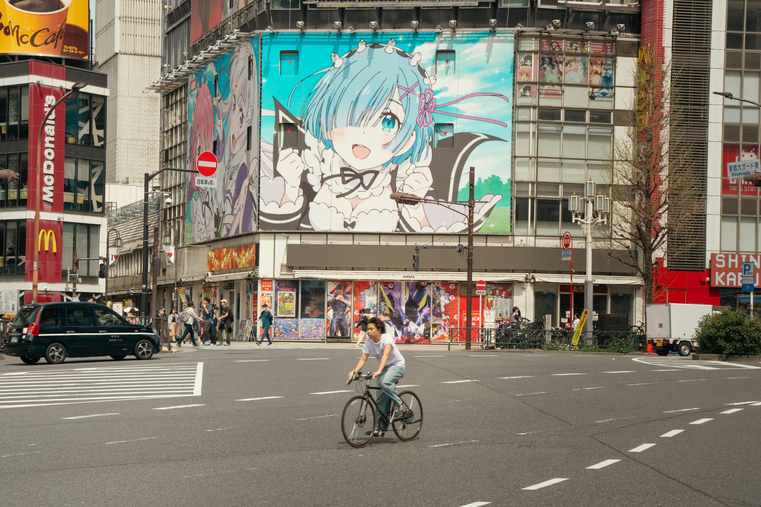 Street scene in Tokyo with anime billboard and cyclist crossing.