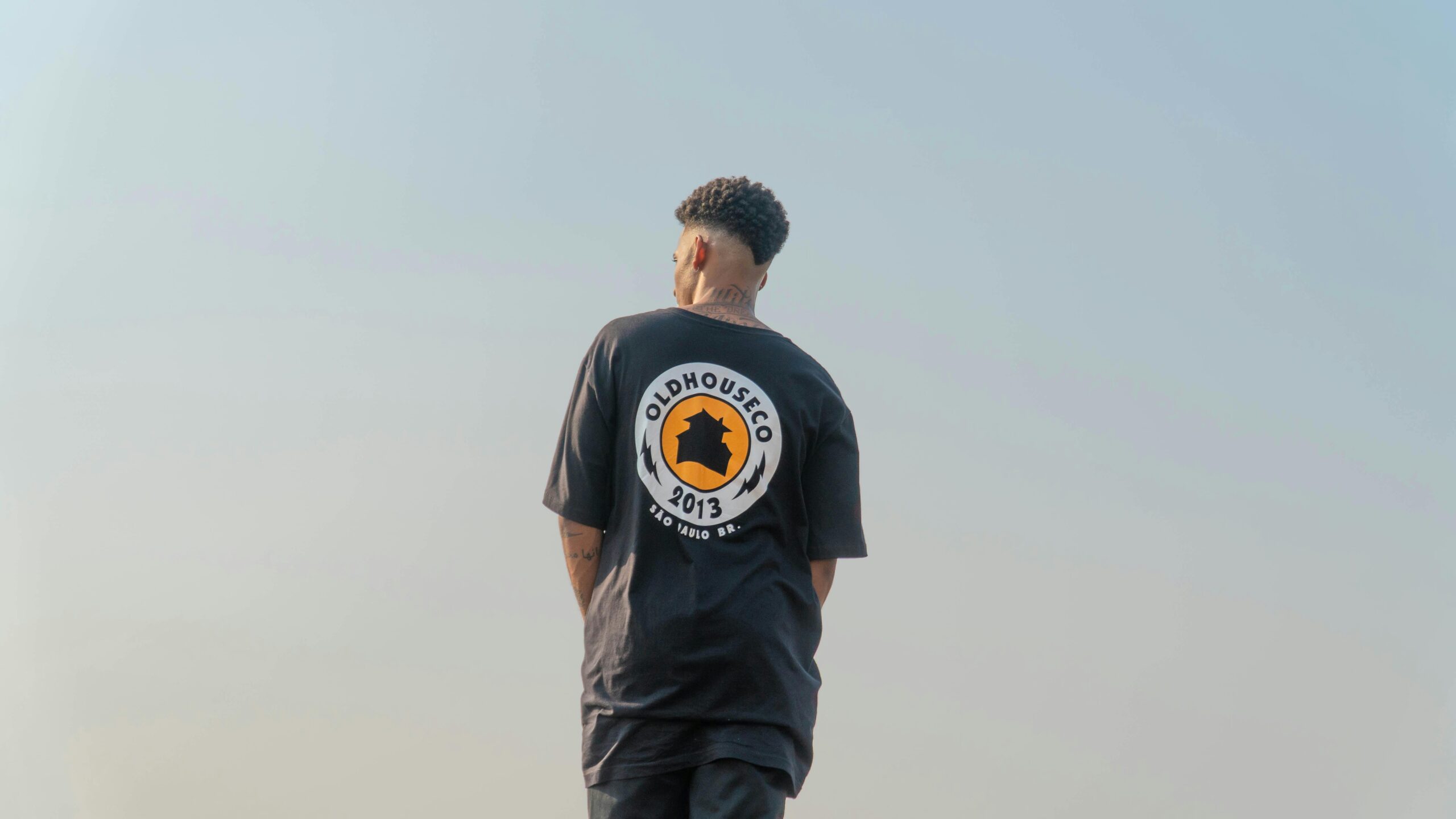 A person in a black shirt with a logo stands outdoors, showcasing a modern style.